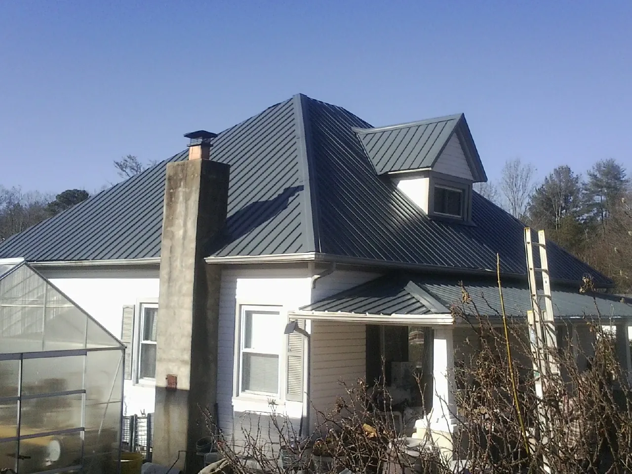 Dark blue standing seam metal roof on a white farmhouse with dormer — Slate & Tile Roof Repair by Roofing Brothers in Wagram