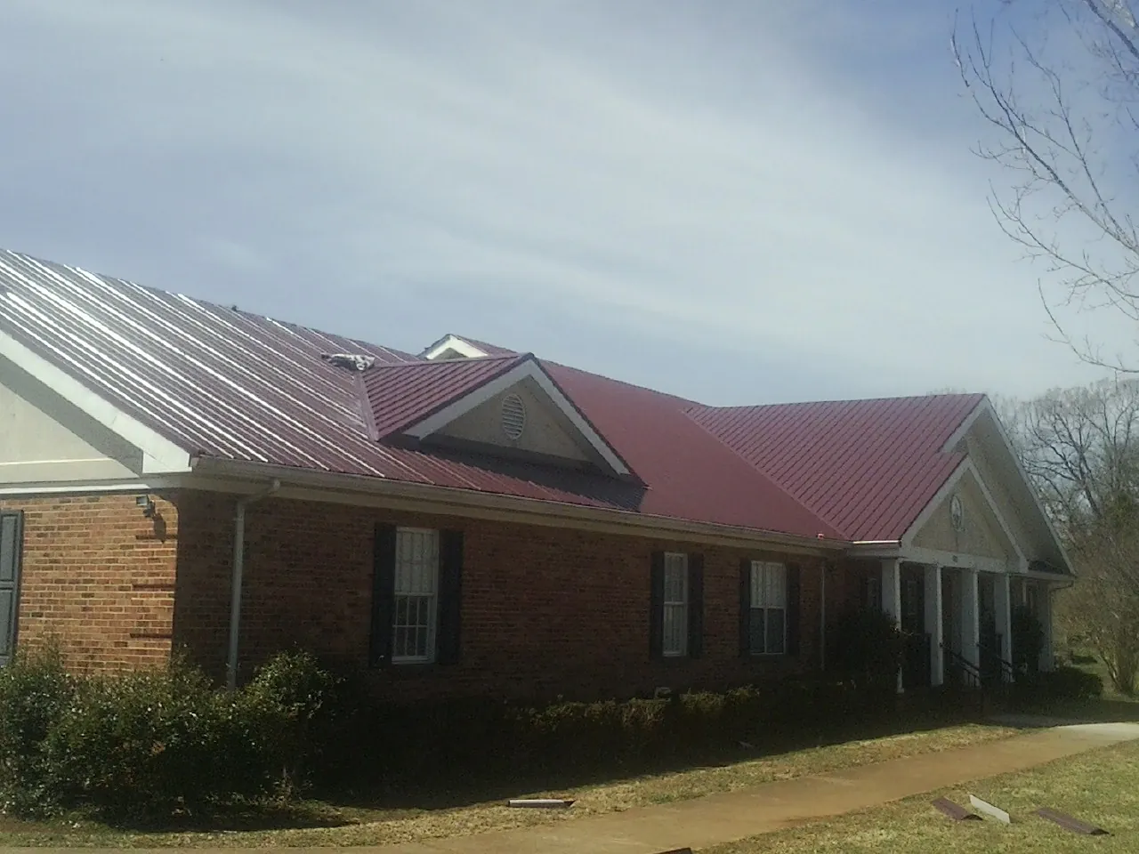 Red metal roof with gabled entries on a long brick building, from a Hail Damage Roof Repair job in Wagram