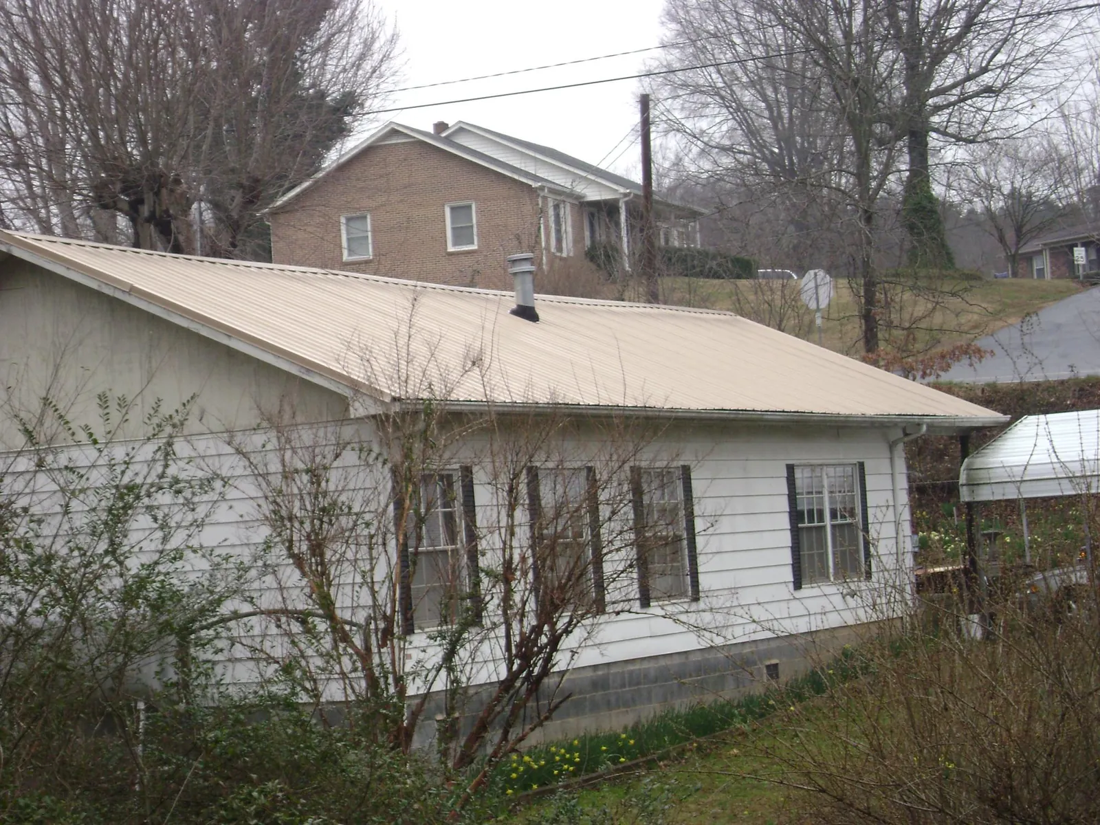 Tan metal roof on a white sided house set into a hillside — Commercial Roofing by Roofing Brothers in Wagram