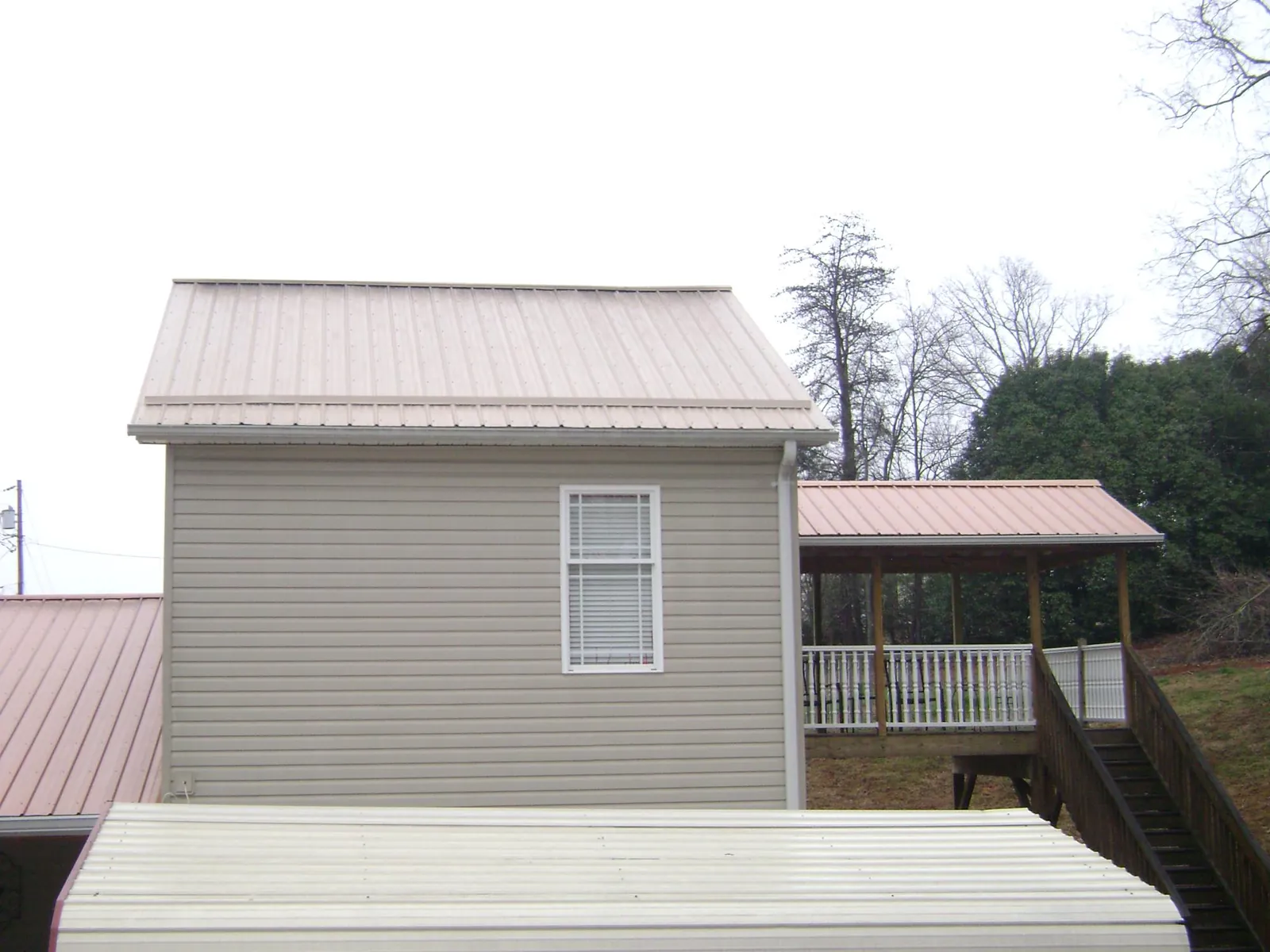 Tan metal roofs on a two story addition and attached porch, from a Roof Replacement job in Wagram